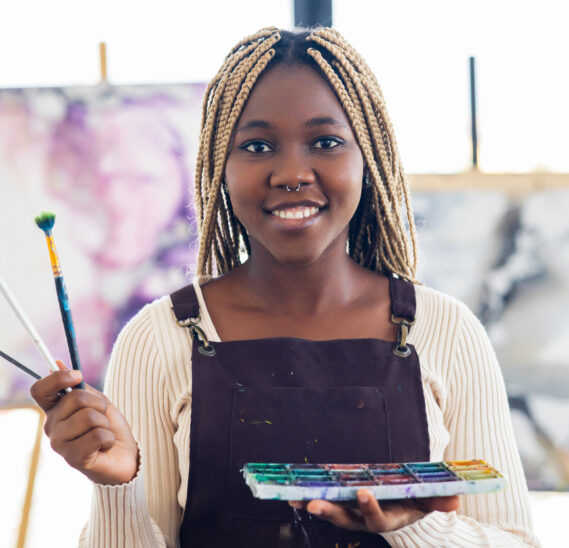 Black student with art scholarship standing with artist's brushes in her hand