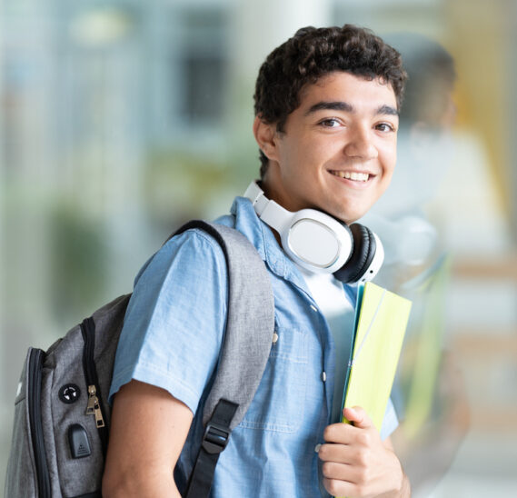 Portrait of positive cheerful hispanic college student holding folders. Teenager boy looking at camera